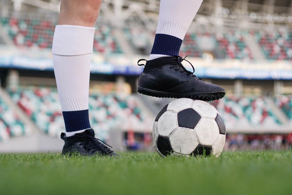 Foto de una persosona con guaybos y un balón de fútbol sobre su pie derecho