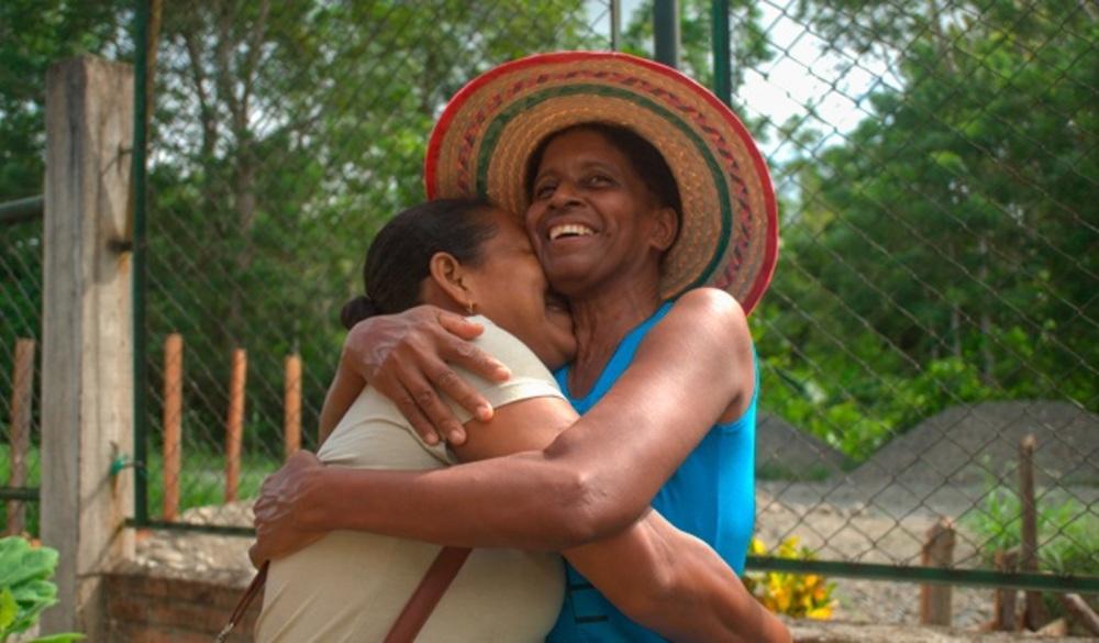 Mujeres abrazandose, una de ellas tiene un sombrero colorido